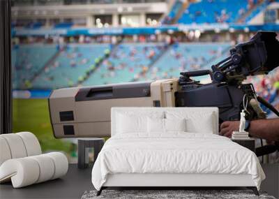 Close-up of a professional television camera in a football stadium, controlled by the hand of a man. Video camera for live coverage of major sporting events Wall mural