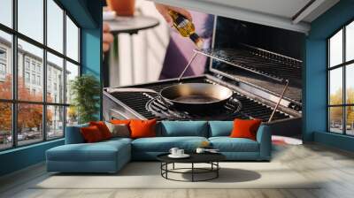 Close-up of man add olive oil on frying carbon steel pan which is on the grill.  Wall mural