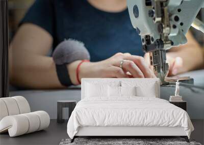 Close up view of sewing process. Female hands stitching white fabric on professional manufacturing machine at workplace. Seamstress hands holding textile for dress production. Wall mural