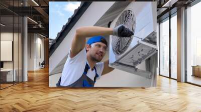 Experienced craftsman with smile tightens bolts body air conditioner unit under roof of building with a screwdriver. Reliable installation of outdoor air conditioning on the facade of the building Wall mural