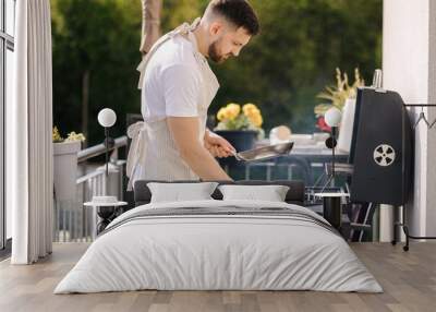 Handsome bearded man hold carbon steel pan and preparing for frying meat on grill Wall mural