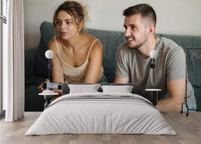 Handsome boy with his fiancee playing video games using joysticks. Man teaches her girlfriend how to play console Wall mural