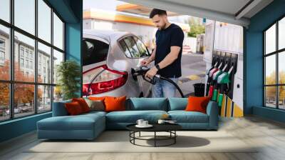 Handsome young man refueling car at gas station. Male filling diesel at gasoline fuel in car using a fuel nozzle. Petrol concept. Side view Wall mural