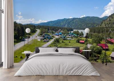 Aerial view of country houses in the village near the highway and the river against the backdrop of the mountains under the blue sky on a warm summer summer day. Picturesque landscape on vacation. Wall mural