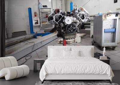 Closeup of a eight cylinder auto engine on a special red stand in a car workshop. Disassembled part during repair in service against the background of a blue car lift. Wall mural