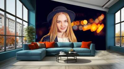 Lovely woman with long hair in a hat on a background of the night city. Close-up. Wall mural