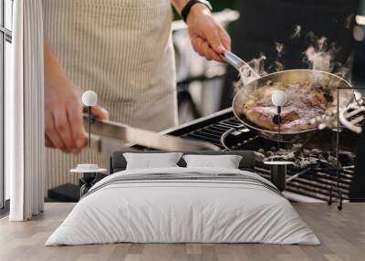 Male chef preparing T-bone steak on carbon steel frying pan outdoor on grill. BBQ concept. Close-up Wall mural