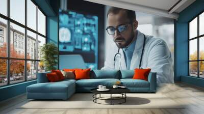 A doctor is sitting at a computer with a laptop open and a monitor in front of him. He is wearing a white lab coat and glasses Wall mural