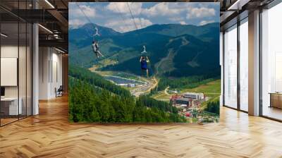 mountain landscape - two tourists fly on a cable on suspensions through a deep abyss against the backdrop of mountain snowy peaks of the Caucasus Mountains Wall mural