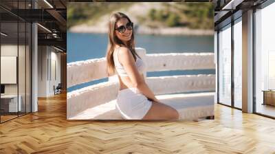 Portrait of young attractive woman in white clothes and sunglasses in front of beautiful sea. Vocation concept Wall mural