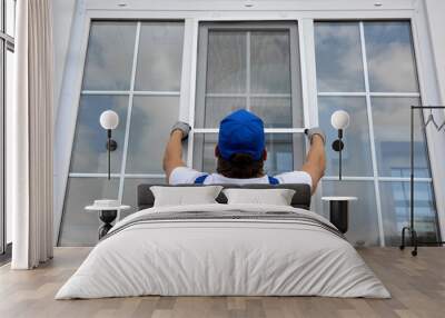 Professional craftsman outside the building installs a mosquito net on large window that lifts it up. Installation of protective net on white plastic window in summer Wall mural