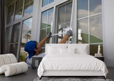 Professional window installer outside the building installs a protective insect net on large plastic window. Working man holds a mosquito net in his hands, compares the size with window Wall mural