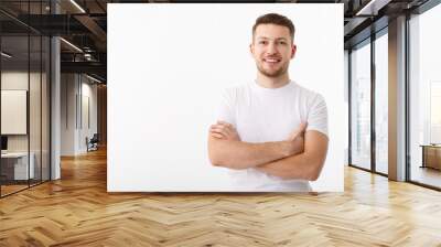 Portrait of a cheerful young man in a white T-shirt on a white background. The guy is standing looking at the camera and smiling. Wall mural