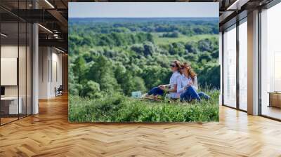 Two girls sit with their backs to each other in nature on picnic. Wall mural