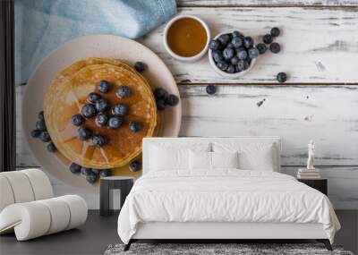 Close up of fluffy pancakes with maple syrup and blueberries against white wooden background Wall mural