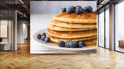 Close up of fluffy pancakes with maple syrup and blueberries against white wooden background Wall mural