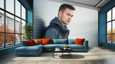 Portrait of a serious young handsome caucasian guy in a black vest opposite steel roll doors on the street in spring. Wall mural