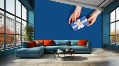 Gift box with surprise in a female hands on classic blue background. Flat lay, top view, place for text. Wall mural