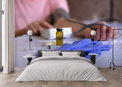 An elderly woman measures blood pressure. On the table is a syringe, a vaccine and a tanometer. Covid-19. Wall mural