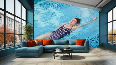 Beautiful adult woman in striped swimsuit swimming in blue pool on her back at resort. Sport activity health concept. Wall mural