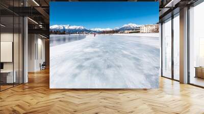 Frozen lake with snowcovered mountains in the background skaters gliding on the ice crisp and clear winter day peaceful and refreshing blue and white palette Wall mural