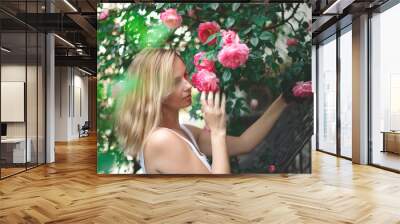 blond woman smiling in a flowering bush of pink roses Wall mural