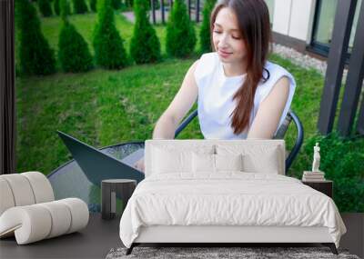 young woman lounges outdoors working on laptop. The relaxed casual vibe captures essence of remote work-life balance. Ideal for lifestyle and productivity themes. Wall mural