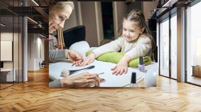 Happy beautician doing manicure to little smiling girl under the gold lamp in the nail salon. Child getting a nail manicure. Wall mural