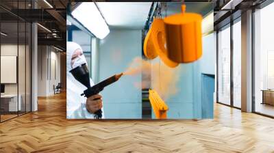 Powder coating of metal parts. A woman in a protective suit sprays powder paint from a gun on metal products Wall mural