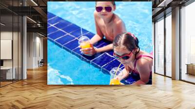 Kids boy and girl holding juice in the swimming pool. Childhood, summer and vacation concept Wall mural