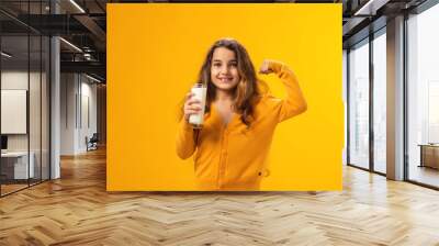 Smiling child girl holding glass of milk and showing strenght gesture. Nutrition and health concept Wall mural