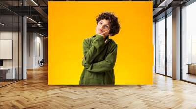 Thoughtful child boy holds chin on yellow background. Dreaming concept Wall mural