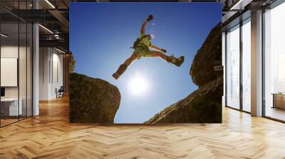 man jumping cliff with blue sky Wall mural