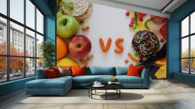 Junk food and healthy food. Red soda or cola can, chocolate doughnut, chips, candies vs green and red apples, grain bread, nuts, orange, lemon, greens. Wall mural