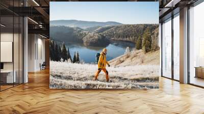 Man with backpack walking on the mountains against the background of an icy lake, mountain trekking in winter, cold season, outdoor vacation, autumn hike. Wall mural