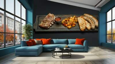 Board with sausages; Ribs, potatoes and sauce for beer isolated on a black background Wall mural