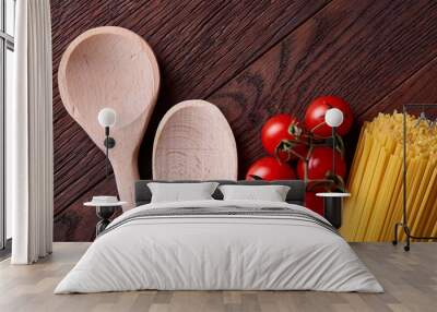 Uncooked pasta, tomatoes and two spoons on wooden background, top view, close-up, selective focus Wall mural