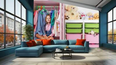 A little child girl is sitting in a wardrobe in a children's room. Saving and storage system for children's things and toys concept. Wall mural