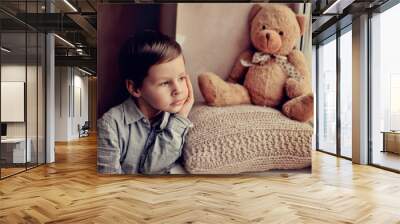 little boy with a toy on a knitted pillow looking out the window Wall mural