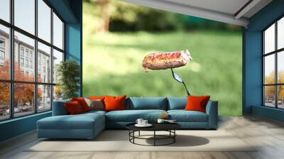 A Bitten off Sausage on a fork with green lawn in background Wall mural