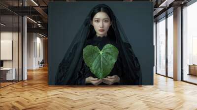 A woman in a black dress holds a green leaf, suitable for use as an illustration or graphic design element Wall mural