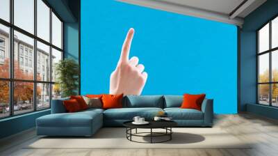 Caucasian white female hand with forefinger raised up and pointing, on blue background, copy space Wall mural