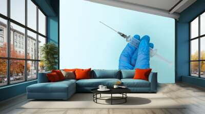 Close-up of a doctor's hand in blue medical gloves holding a syringe with a medicine on a blue background with copy space. The concept of immunization, vaccination and treatment of infection. Wall mural