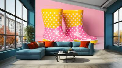 Close up of colorful yellow pink polka dot rubber boots standing in a row. Showcasing beautiful autumn shoes rain boots on a solid pink background Wall mural