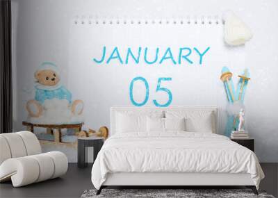 January 5th. Teddy bear sitting on a sled, blue skis and a calendar date on white snow. Day 5 of month. Wall mural