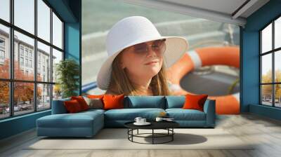 A happy girl in a white hat and a blue swimsuit on the sea beach wearing sunglasses.  a happy child on the ocean. summer vacation. background for the design. Wall mural