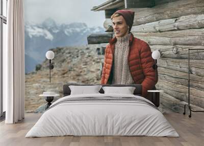 Handsome male model wearing warm sweater and winter coat over mountains with snow Wall mural