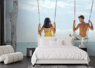 Teenage girl and boy hanging on swings with a sea view in beach cafe Wall mural