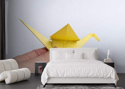 Traditional Japanese origami cranes made of yellow paper on a white background. A hand holding a paper bird. Children's creativity. A symbol of peace. Wall mural