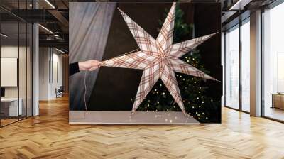 A large decorative star ornament with plaid patterns, hanging beautifully with glowing lights in the background. Ideal for enhancing Christmas or winter decor. Wall mural